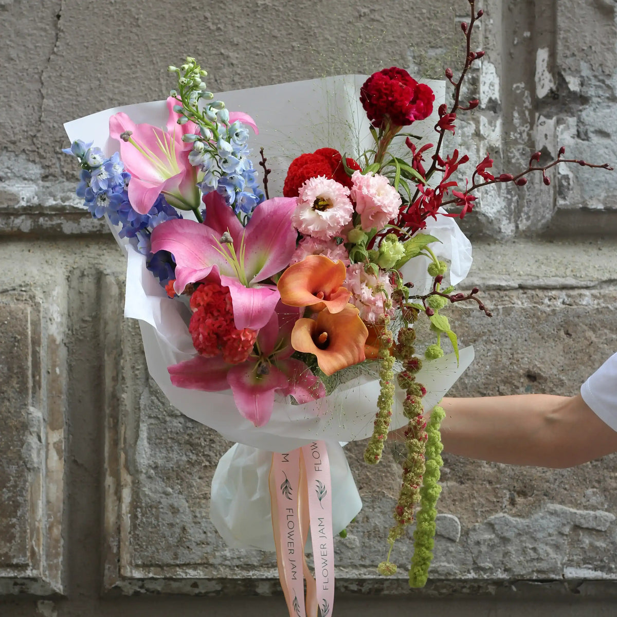 A bouquet of colorful lilis, callas, wil orchids and lisianthus wrapped in white paper.