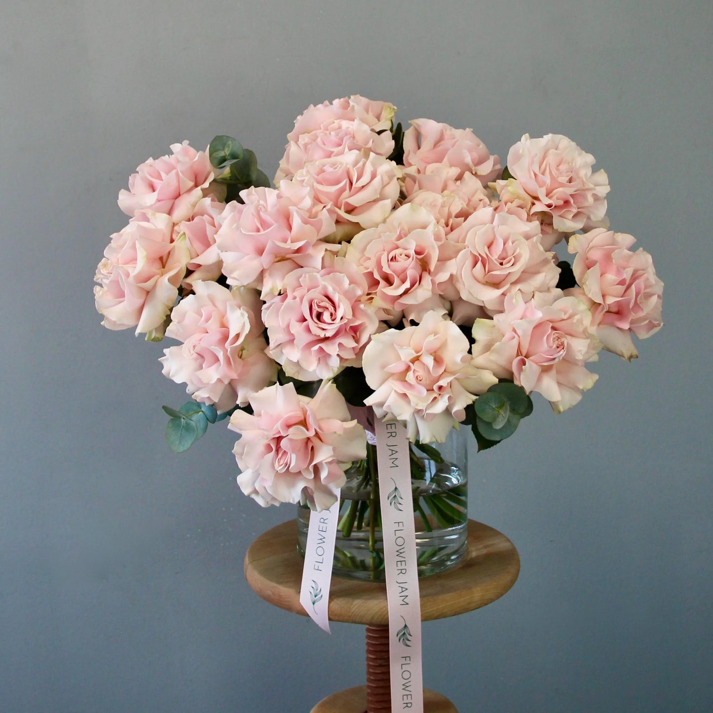 Bouquet of pink flowers in a clear vase on a wooden stand against a gray background
