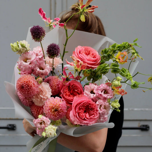Pink gloriosa, pink lisianthus, pink english garden rose, purple  blue and green goodies, put together into a bouquet wrapped by neutral white paper