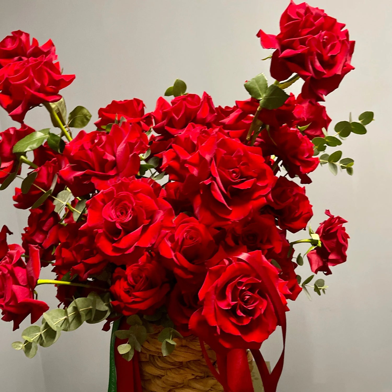 Bouquet of red roses with green leaves in a woven basket against a neutral background
