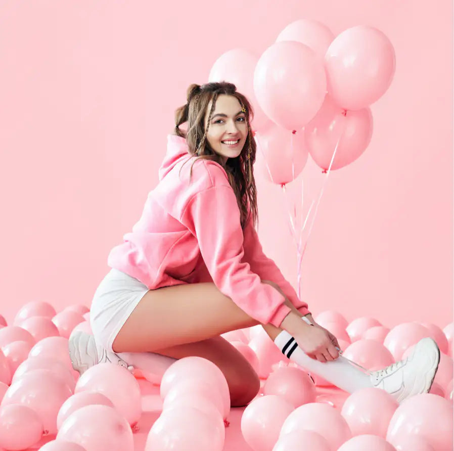 girl dressed in pink sits in the middle of pink balloons with pink background