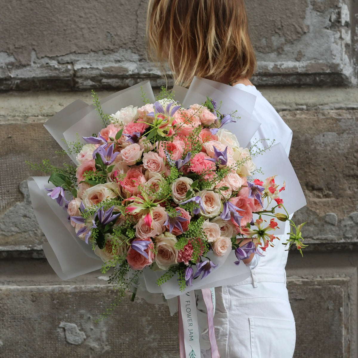A woman dressed in white, holding a bouquet of mix of roses, climatis, gloriosa and goodies.