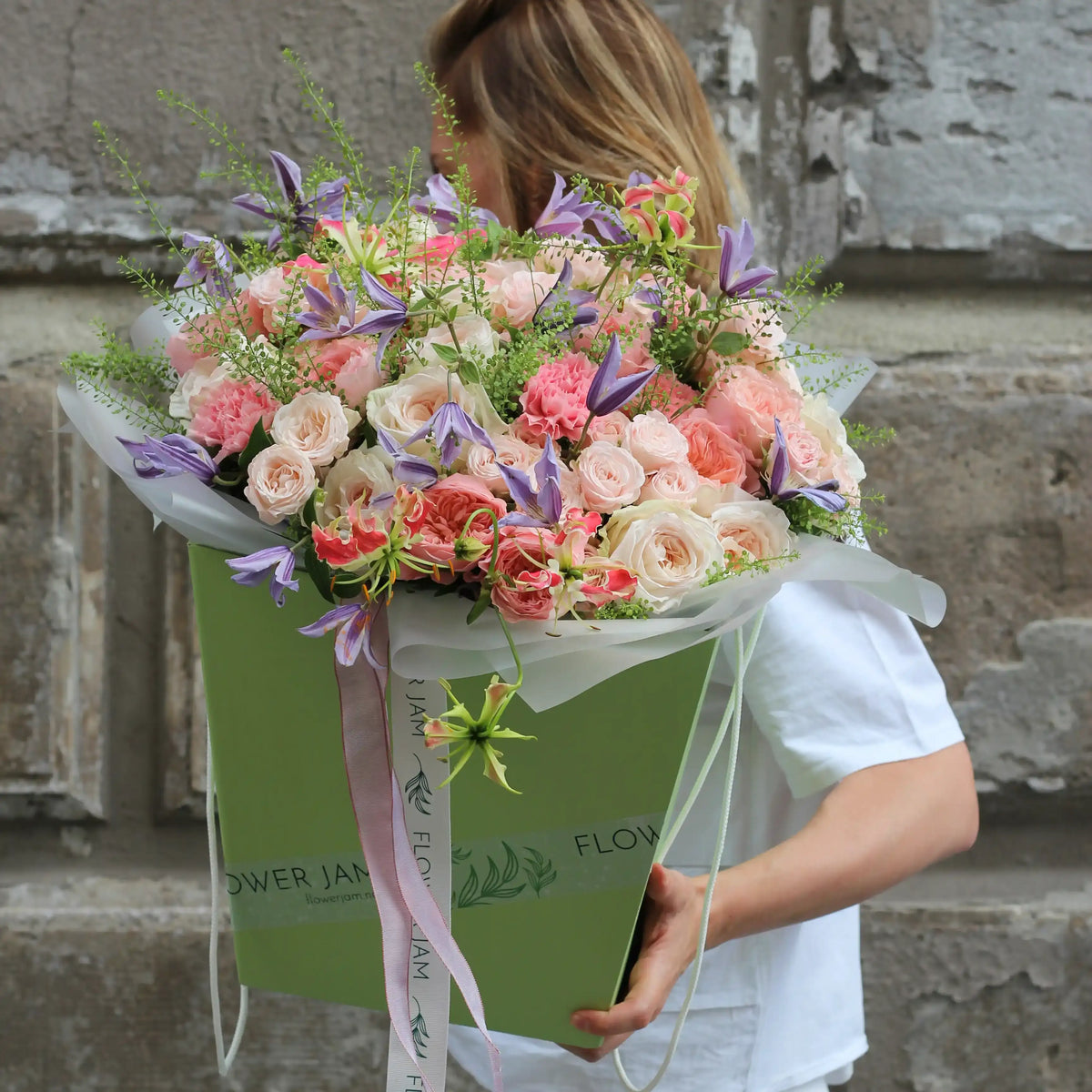 A green transportation box with a big colorful bouquet of pink roses, pink carnations, purple clematis and pinkk gloriosa.