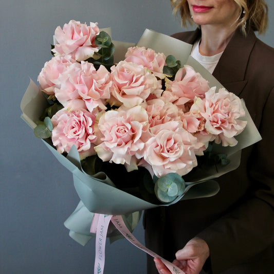 Bouquet of pink roses held by a person against a gray background