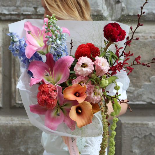 Bouquet of vibrant flowers such as lilies, callas, celosia, delphinium, hydrangea, wild orchids and amaranthus.