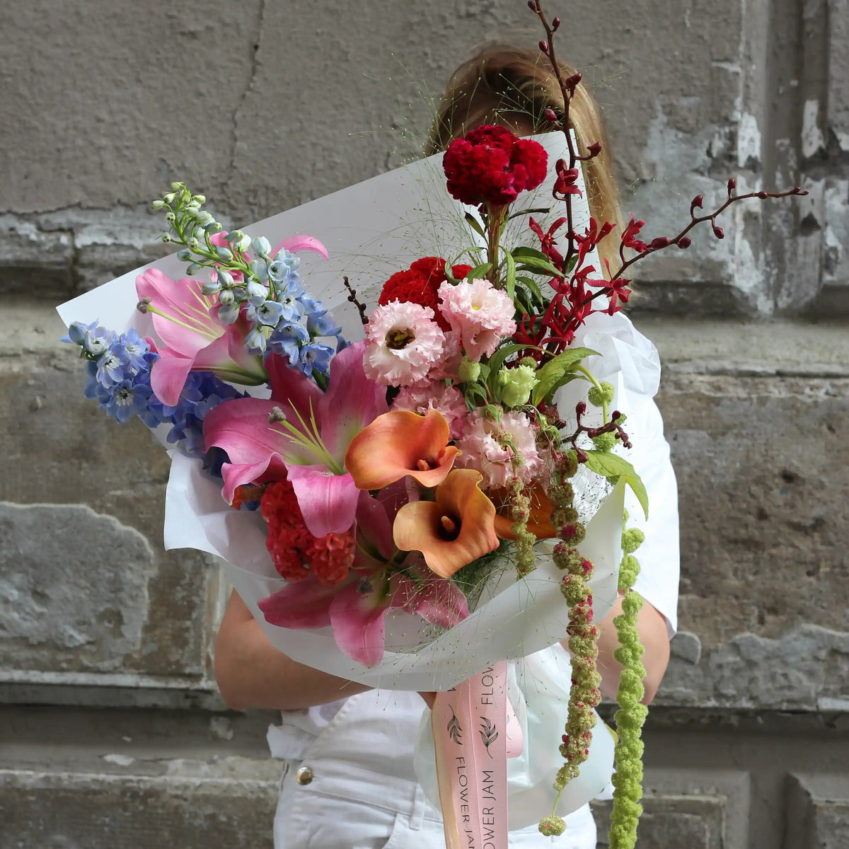 A woman dressed in white is holding a colorful bouquet of pink, orange, red, blue and green flowers.