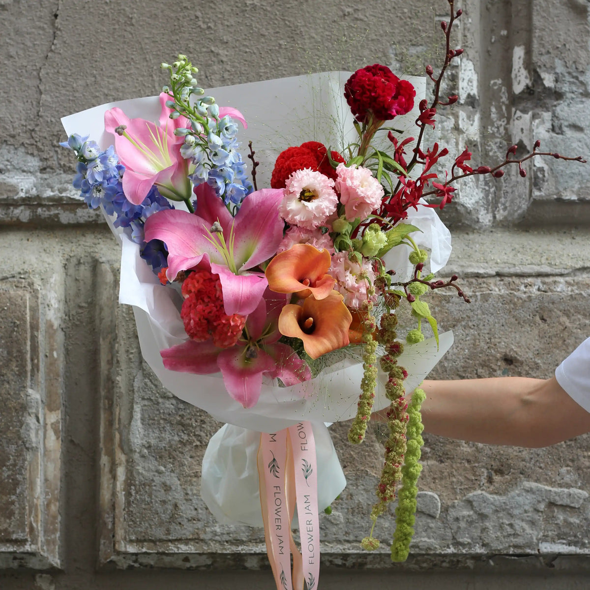 A bouquet of colorful lilis, callas, wil orchids and lisianthus wrapped in white paper.